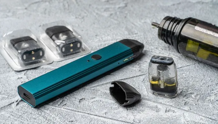 Dispositif de vapotage moderne en turquoise avec cartouches de rechange sur un fond de béton gris. L'image montre une cigarette électronique rechargeable et ses pods interchangeables, soulignant la commodité et la facilité d'utilisation des systèmes de vapotage modernes.