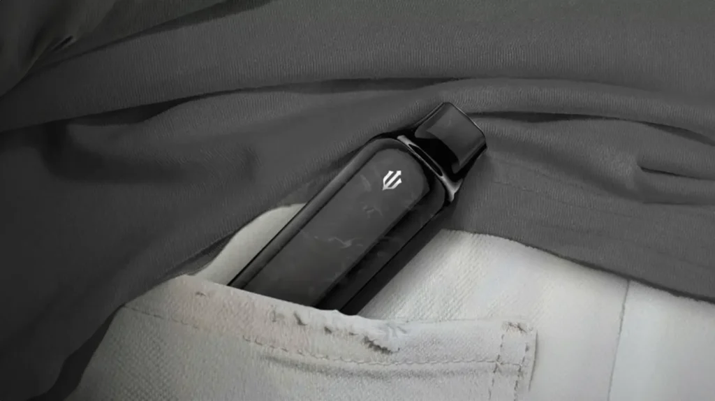 Cigarette électronique jetable EMIRY Aura Mini de couleur noire, discrètement rangée dans la poche d'un pantalon gris. Cet appareil compact et élégant est parfait pour une utilisation nomade, offrant une solution pratique et stylée pour les vapoteurs qui préfèrent une discrétion maximale sans compromettre la performance.