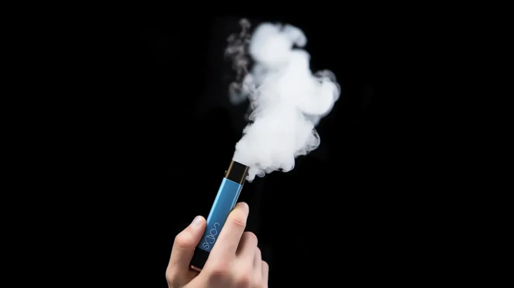 Main tenant une puff bleue produisant de la vapeur dense, avec un fond noir, illustrant l'utilisation d'une cigarette électronique.