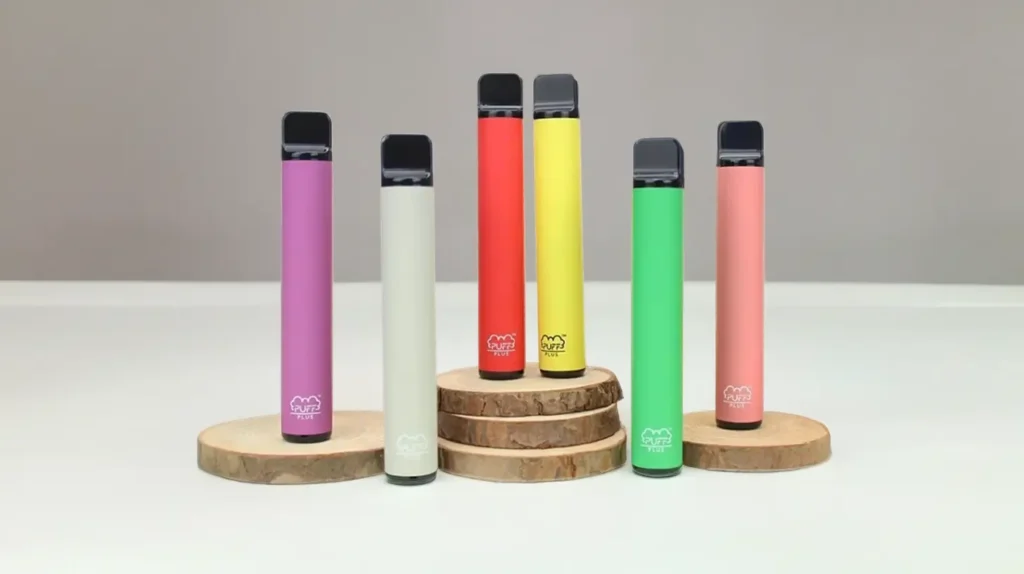 "Collection de Puff Bar Plus colorées sur des supports en bois" - Un assortiment de Puff Bar Plus disposées debout sur des socles en bois, chaque appareil présentant une couleur différente qui indique sa saveur unique. L'image met en avant la diversité et la portabilité des produits Puff Bar Plus.